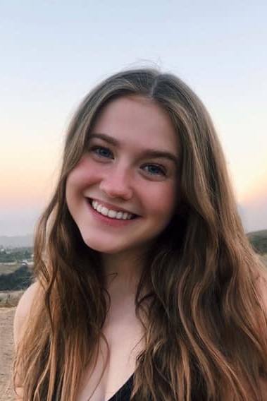 Young woman smiling outdoors during sunset.