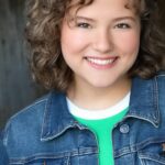Smiling woman with curly hair wearing a denim jacket.